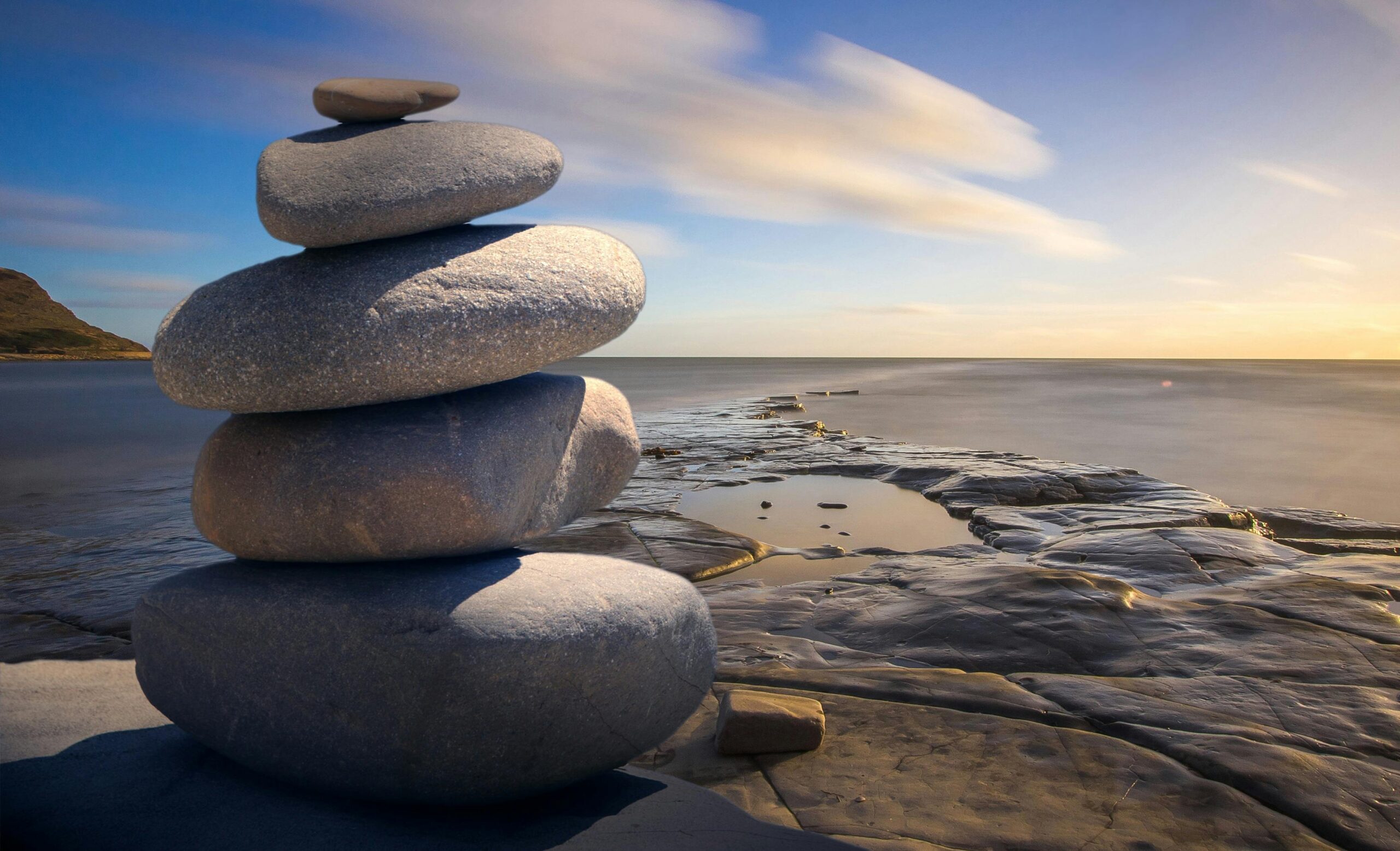 COACHING: COS'È, BENEFICI E DIFFERENZE CON LA TERAPIA A serene stack of stones on the rocky seashore during a peaceful sunrise, embodying balance and zen.