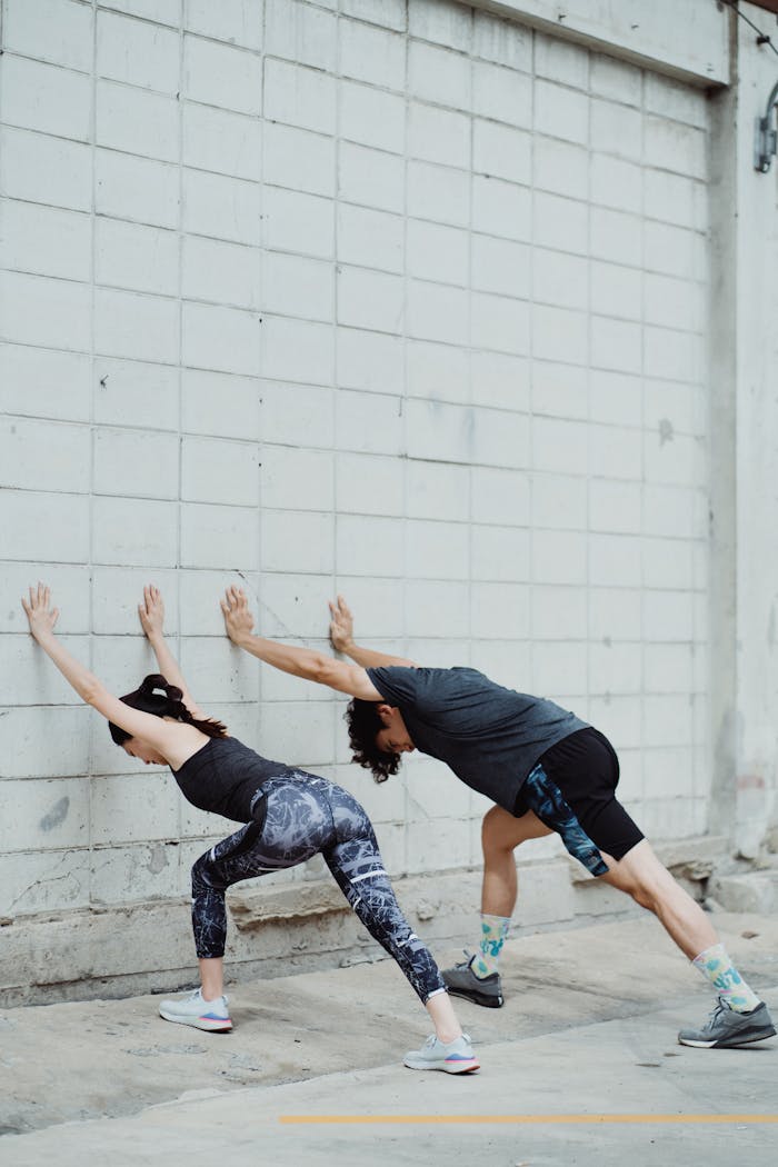 how-we-are Two athletes stretch against a concrete wall outdoors for fitness training.