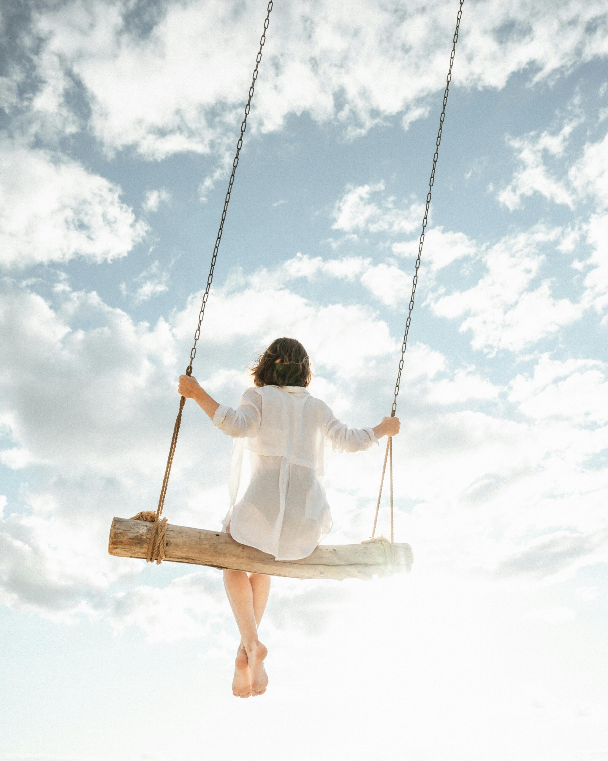 EFT INTEGRATA: LIBERARSI DALLE EMOZIONI BLOCCATE E RITROVARE L'EQUILIBRIO A woman in white swings high in the sky against a backdrop of fluffy clouds.